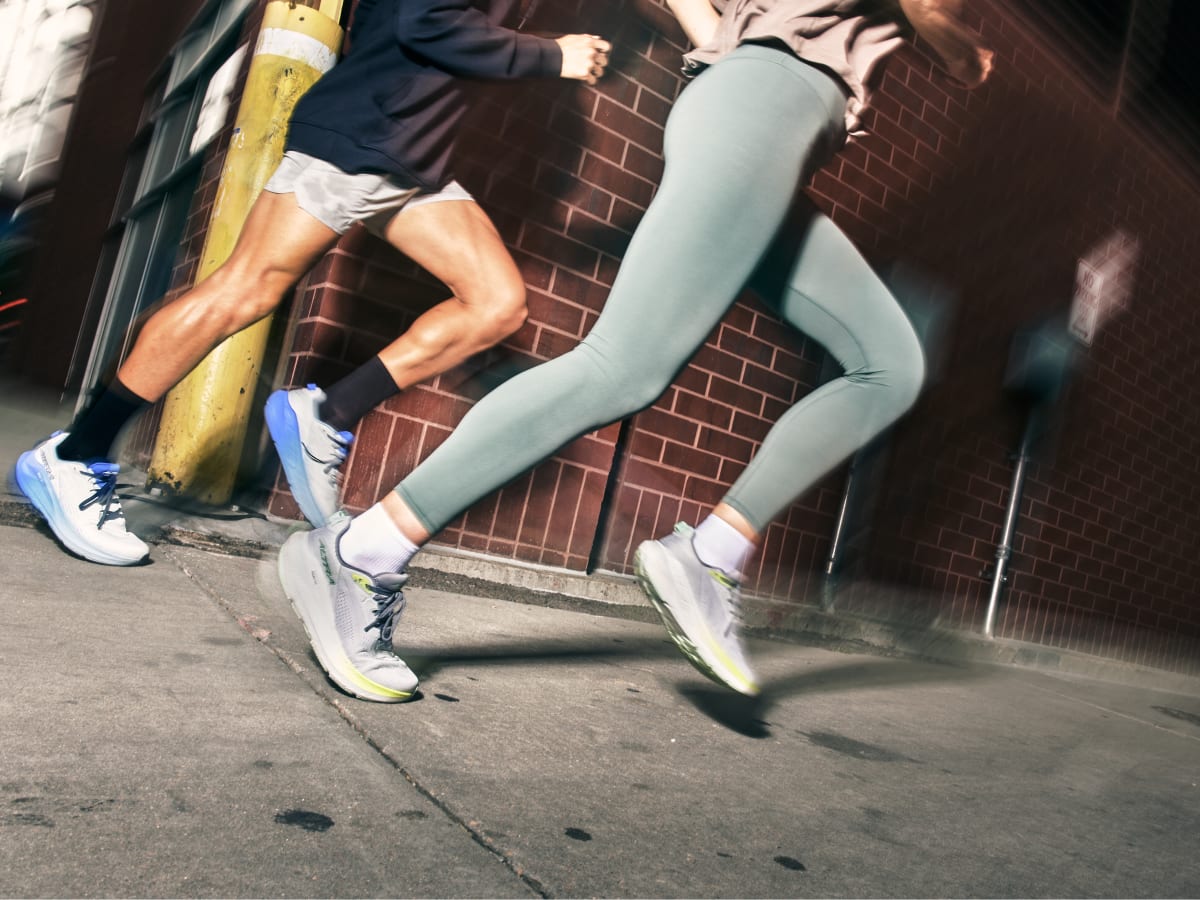Two runners mid‑stride wearing Altra FWD Via 2 on an urban sidewalk, highlighting road running movement in a city environment.
