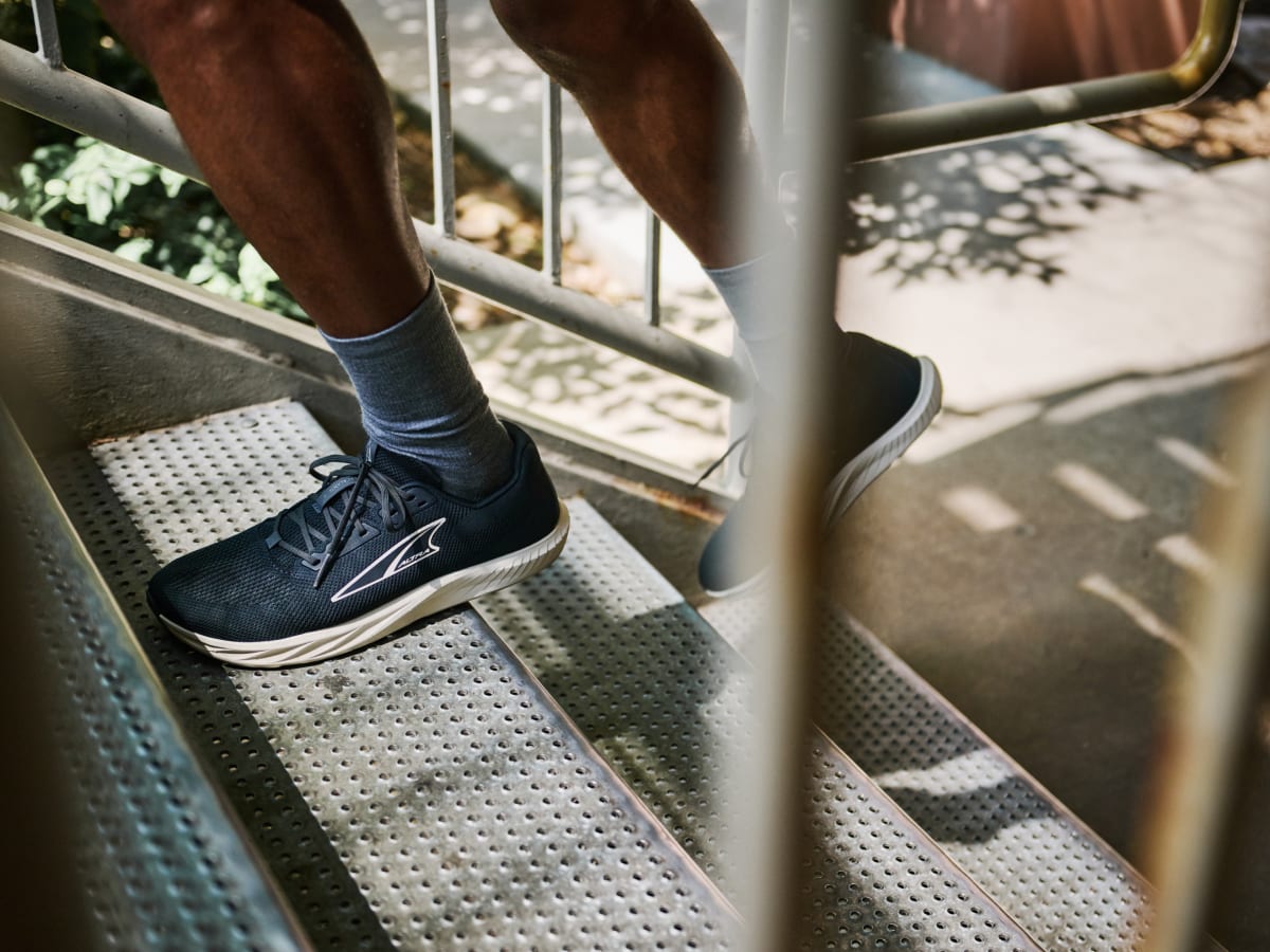 Runner wearing Altra Escalante 4 walking up metal stairs outdoors, showcasing lightweight performance design.