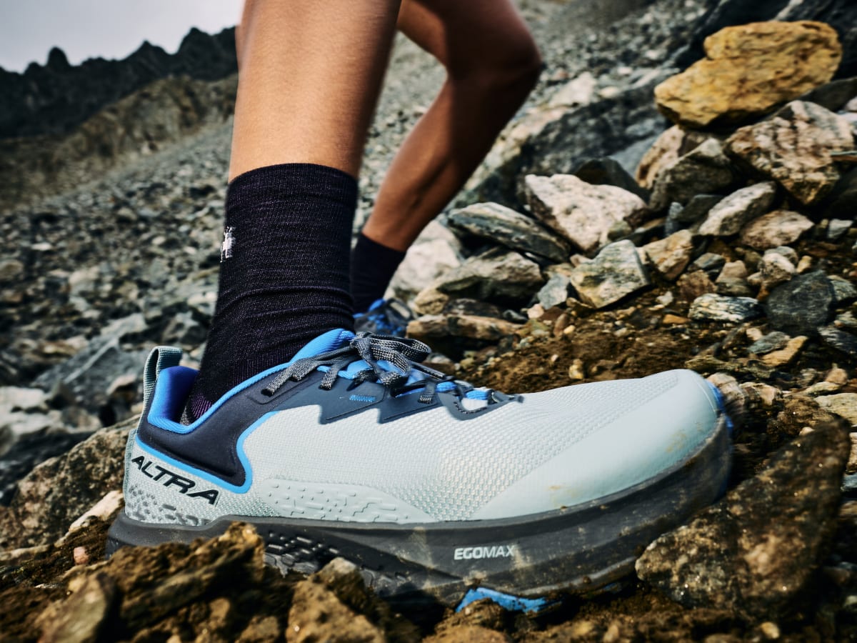 Athlete wearing Altra Timp 6 trail running shoes stepping on rocky mountain terrain, highlighting durable outdoor performance.